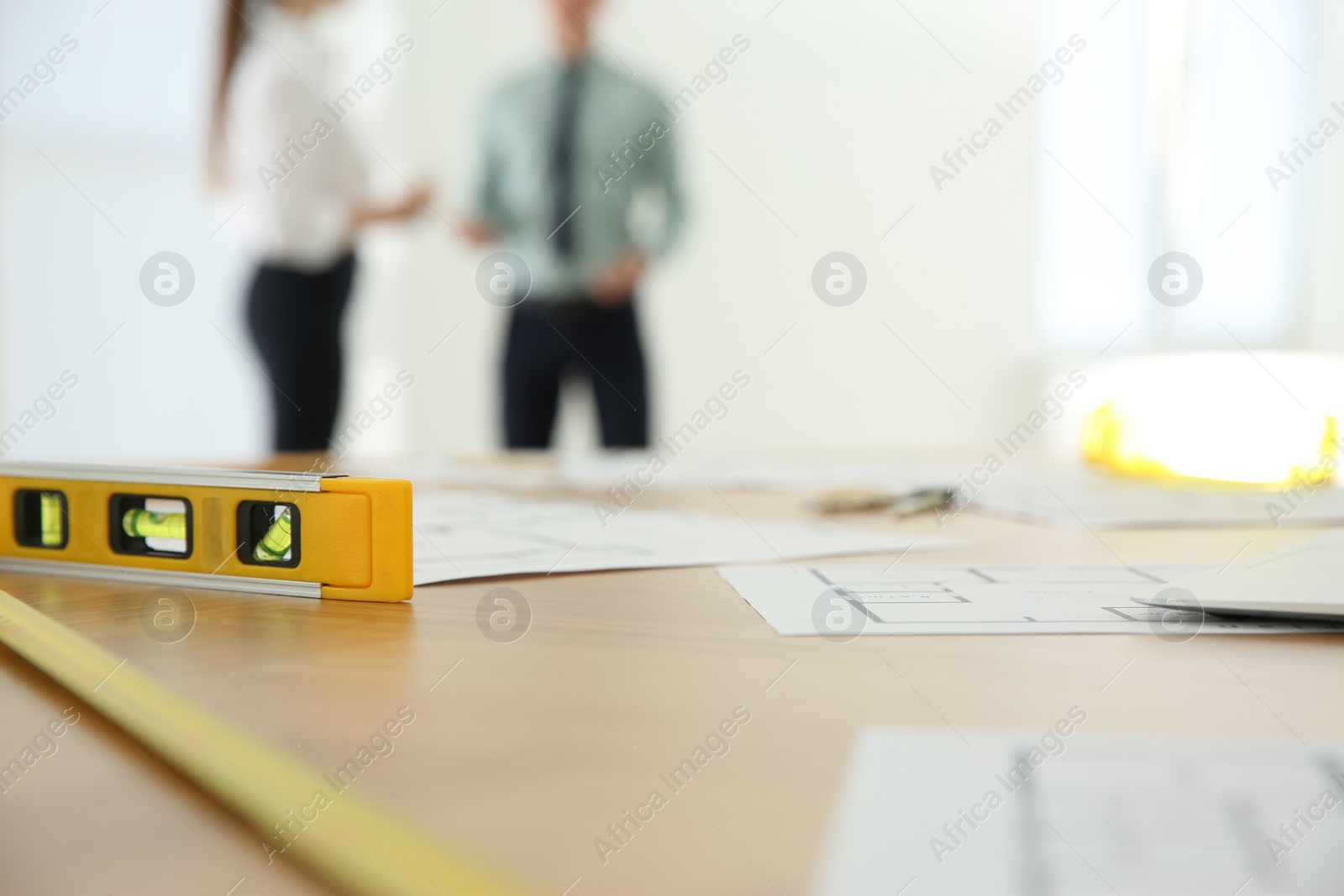 Photo of Colleagues in office, focus on table with construction drawings and tools