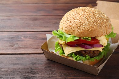 Photo of Delicious burger in cardboard box on wooden table. Space for text