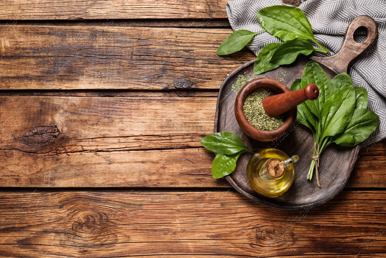 Photo of Fresh and dried broadleaf plantain leaves with essential oil on wooden table, flat lay. Space for text