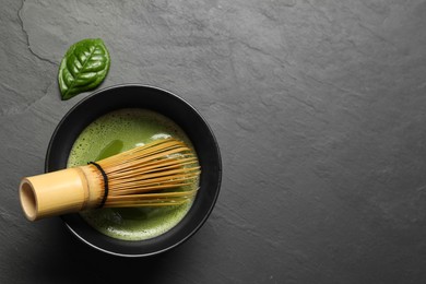 Photo of Cup of fresh green matcha tea with bamboo whisk on black table, top view. Space for text