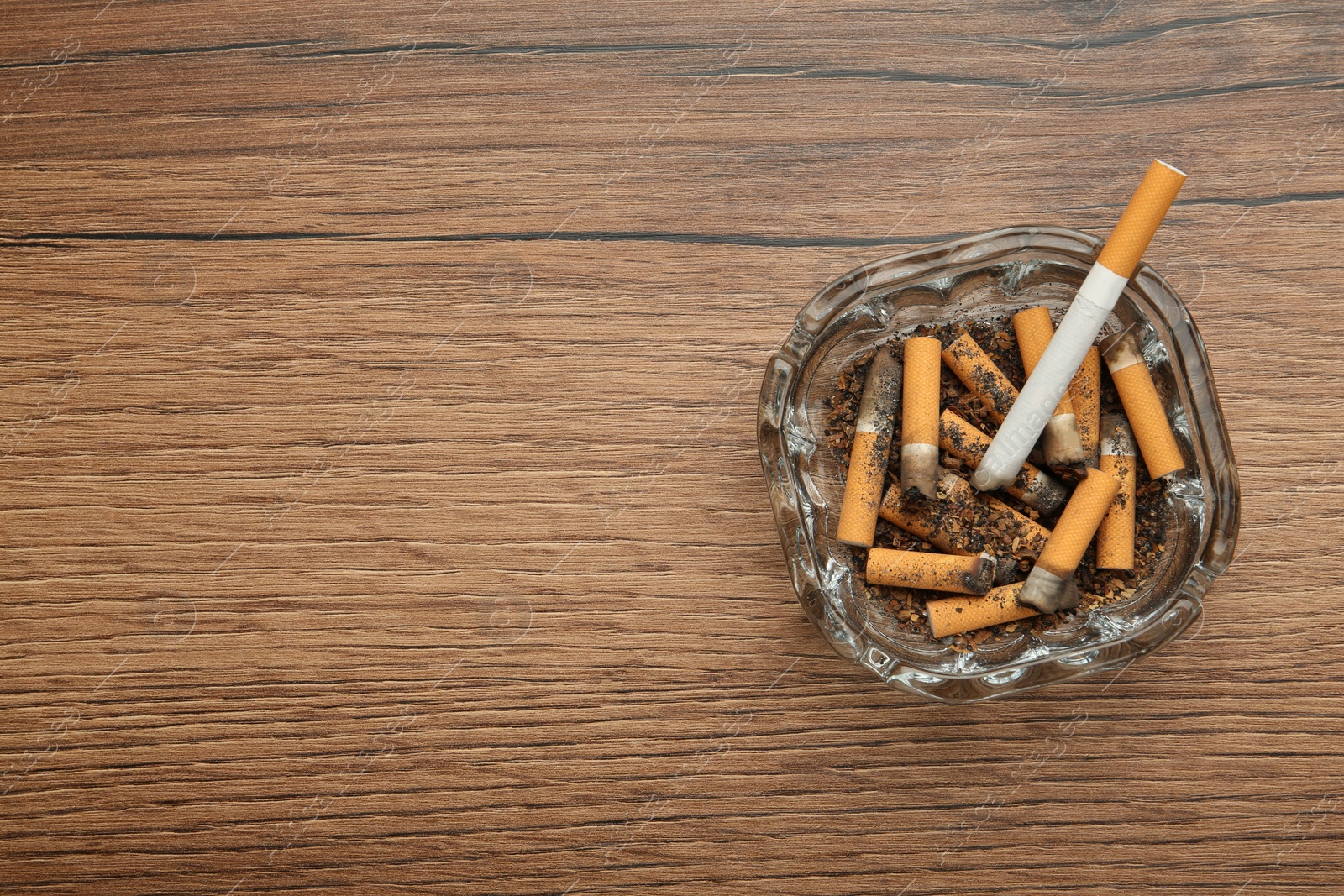 Photo of Glass ashtray with cigarette stubs on wooden table, top view. Space for text