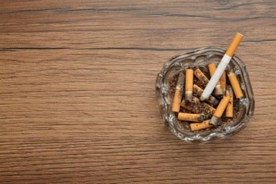 Glass ashtray with cigarette stubs on wooden table, top view. Space for text