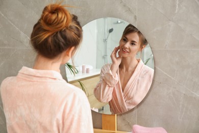 Photo of Beautiful woman wearing pink bathrobe in front of mirror at home