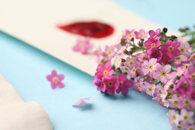 Photo of Beautiful Forget-me-not flowers and envelope on light blue background, closeup
