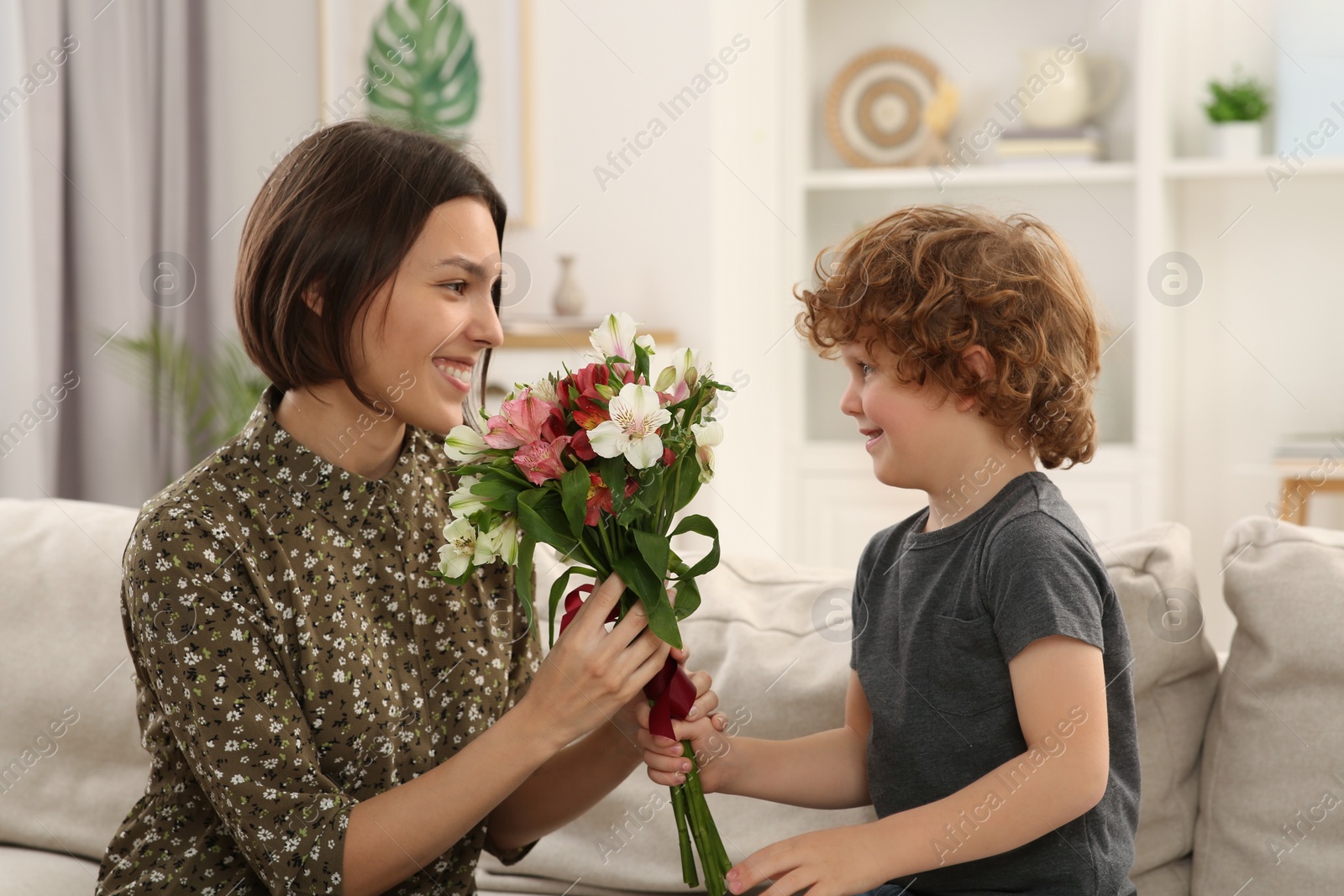 Photo of Happy woman with her cute son and bouquet of beautiful flowers at home. Mother's day celebration