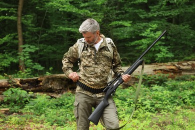 Man with hunting rifle and backpack wearing camouflage in forest