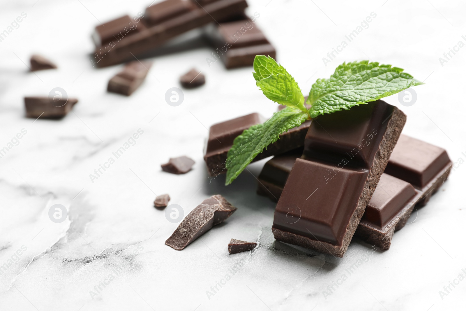 Photo of Pieces of dark chocolate with mint on marble table