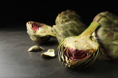 Photo of Cut and whole fresh raw artichokes on grey table, space for text