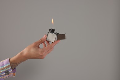Photo of Woman holding lighter with burning flame on grey background, closeup. Space for text