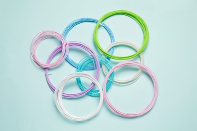 Photo of Colorful plastic filaments for 3D pen on light blue background, flat lay