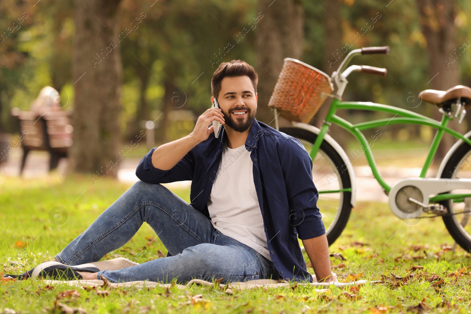 Photo of Young man sitting on green grass near bicycle and talking over smartphone in park