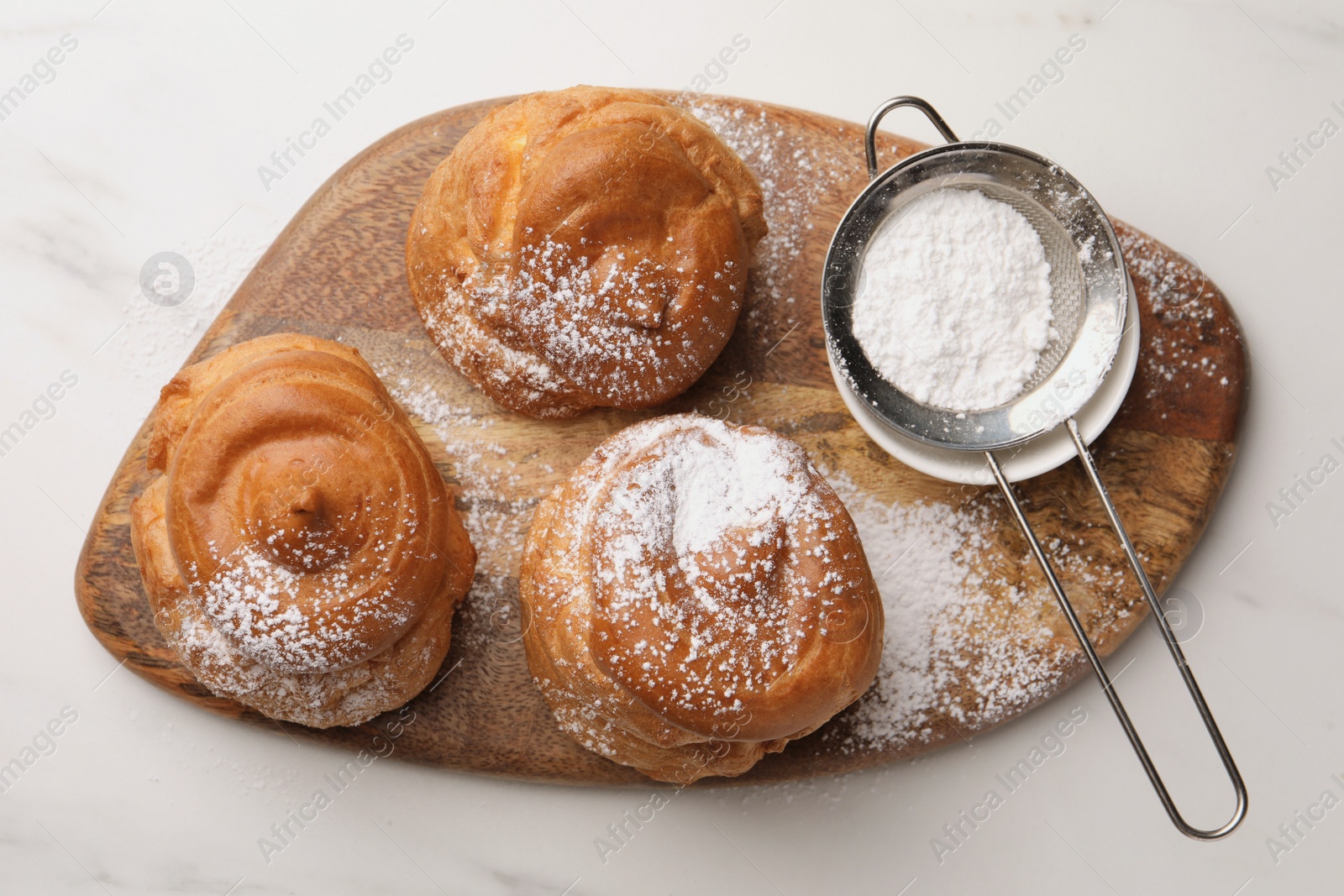 Photo of Delicious profiteroles with powdered sugar on wooden board, top view