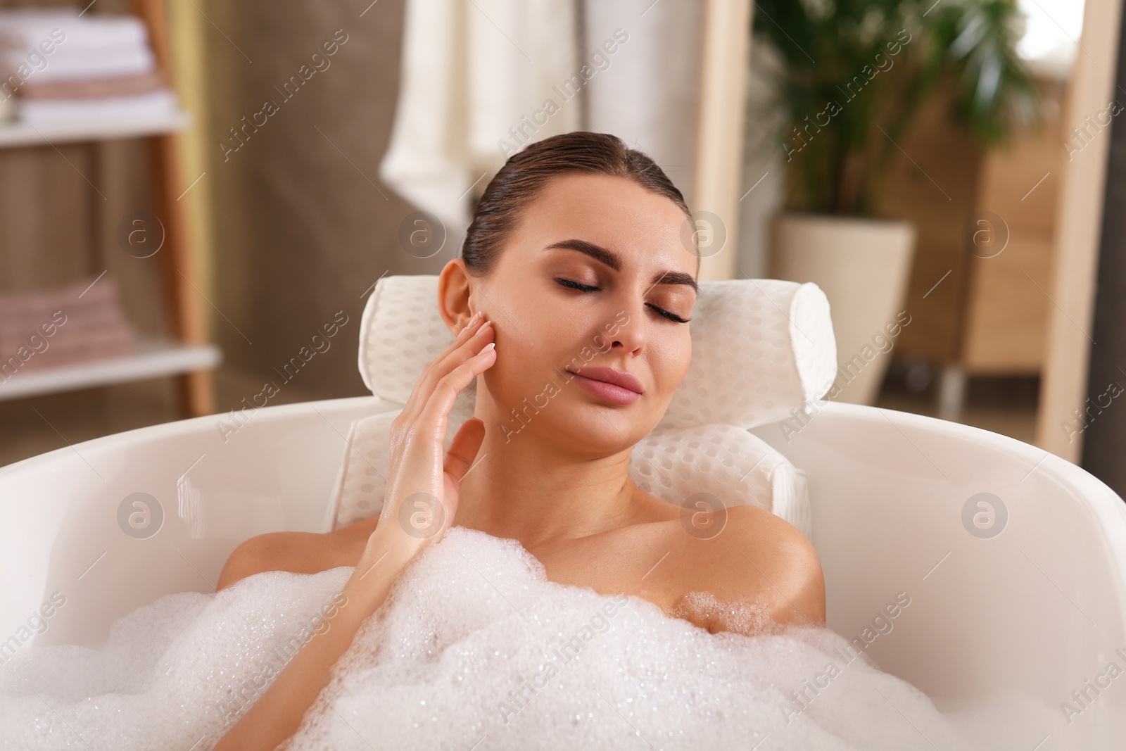 Photo of Young woman using pillow while enjoying bubble bath indoors