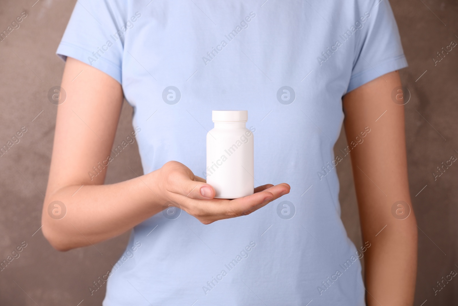 Photo of Woman holding blank white bottle with vitamin pills against light brown background, closeup