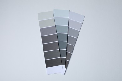 Photo of Color paint chips of grey shades on light background, top view