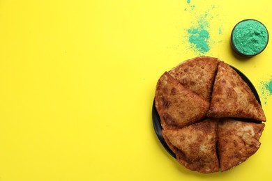 Traditional Indian food and color powder on yellow background, flat lay with space for text. Holi festival celebration