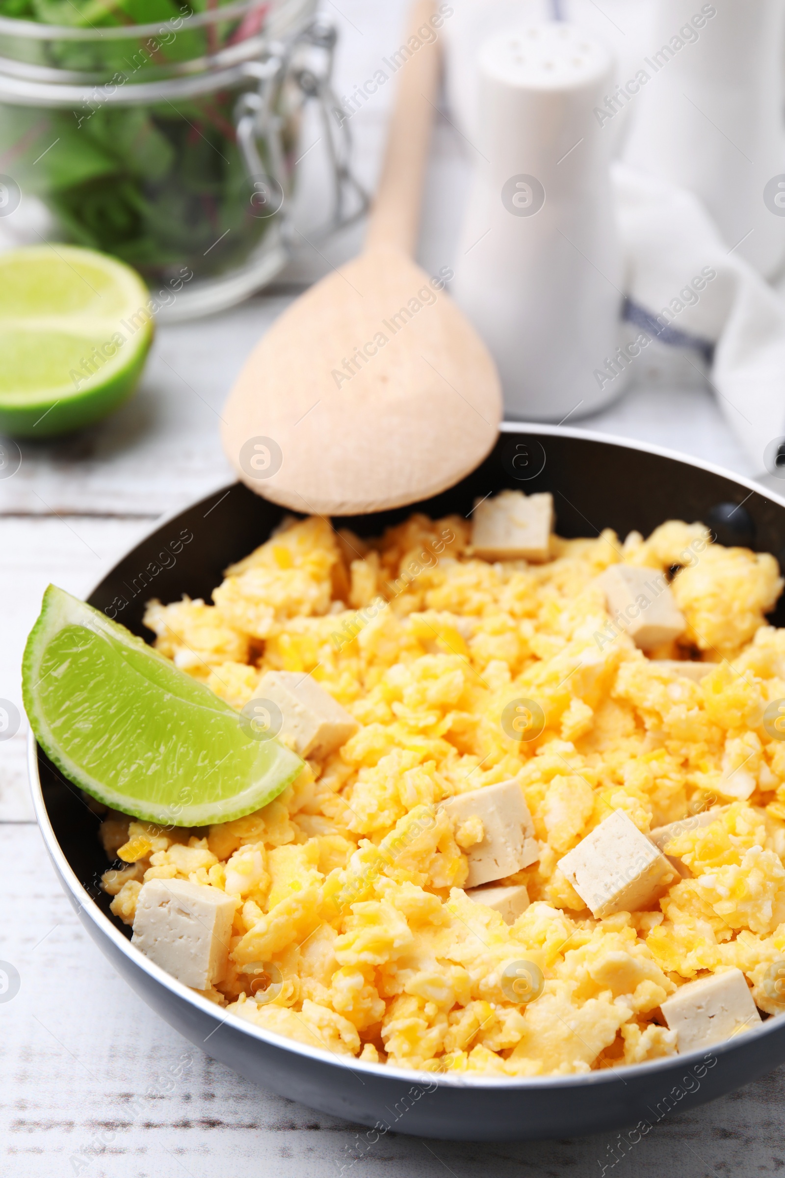 Photo of Frying pan with delicious scrambled eggs, tofu and lime on white wooden table