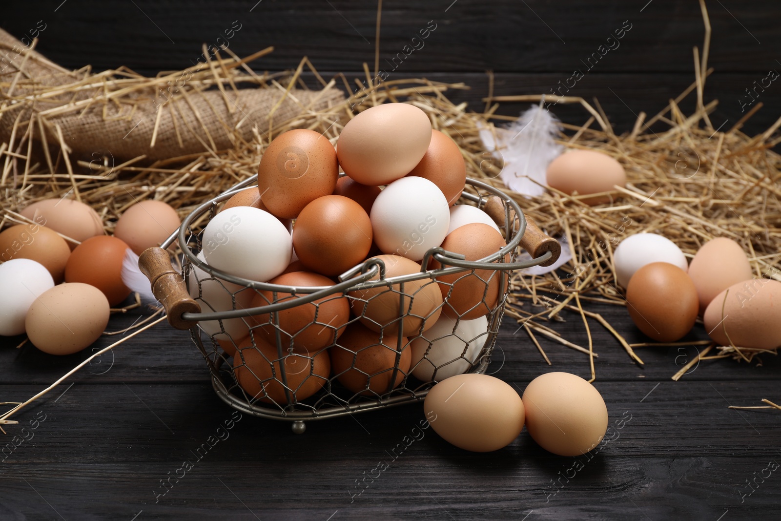 Photo of Fresh chicken eggs and dried straw on black wooden table