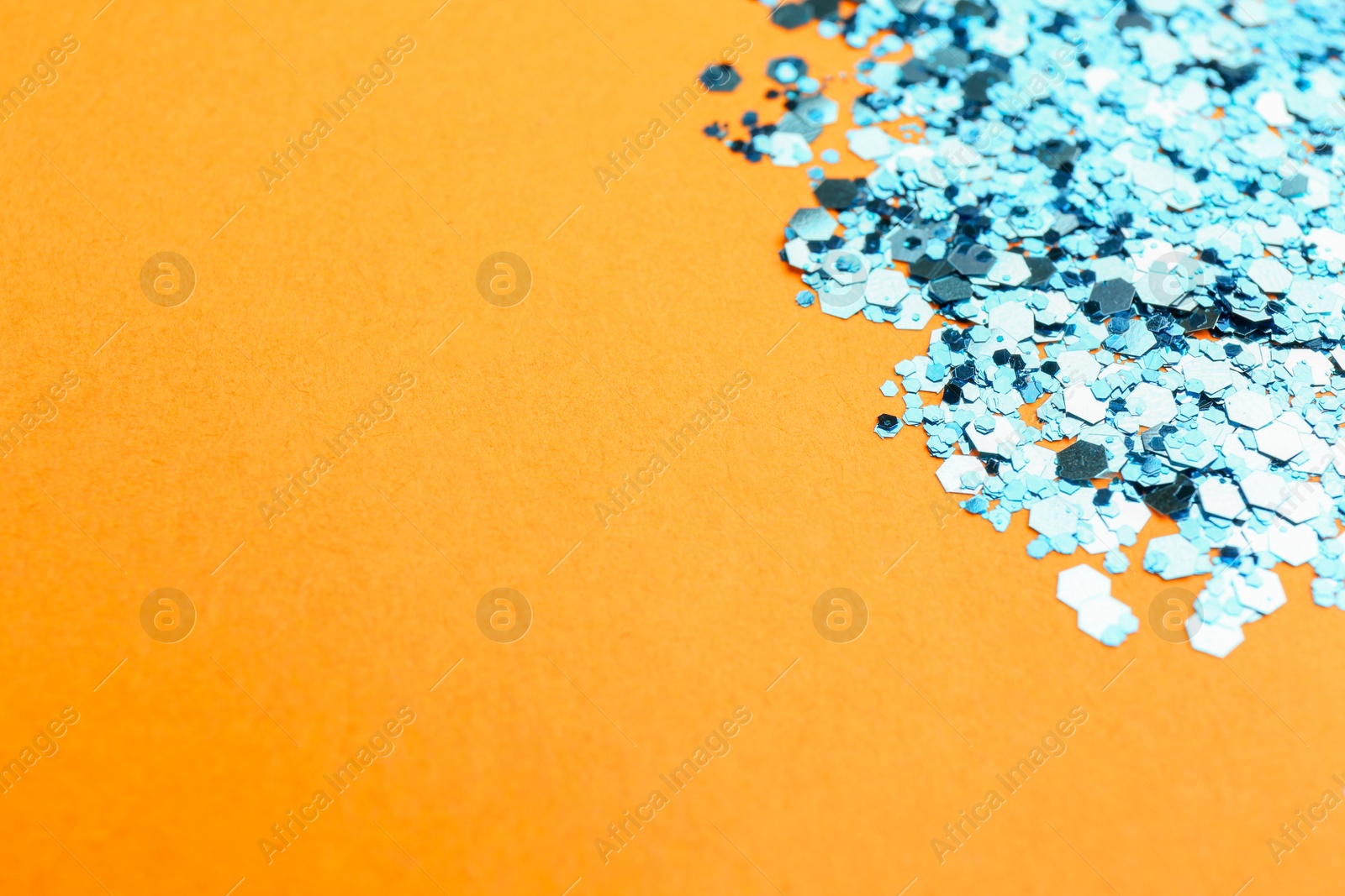 Photo of Shiny bright light blue glitter on pale orange background, closeup. Space for text