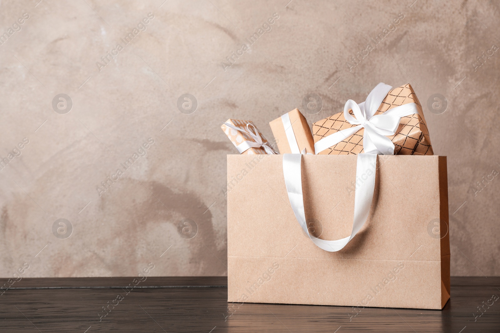 Photo of Paper shopping bag with handles full of gift boxes on table. Mock up for design