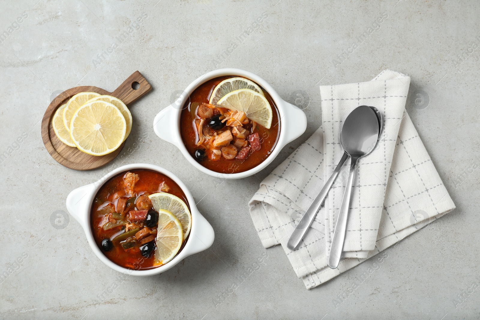 Photo of Meat solyanka soup with sausages, olives and vegetables served on white textured table, flat lay