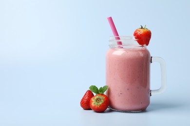 Photo of Mason jar with delicious strawberry smoothie and fresh berries on light blue background. Space for text