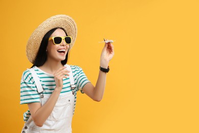 Happy female tourist with toy plane on yellow background. Space for text