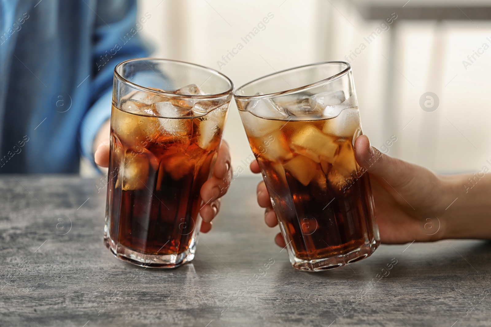 Photo of Women holding glasses of cola with ice at table, closeup