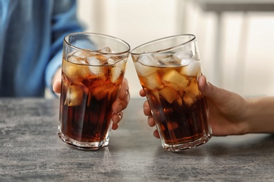 Photo of Women holding glasses of cola with ice at table, closeup