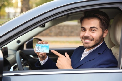 Photo of Young man holding driving license in car