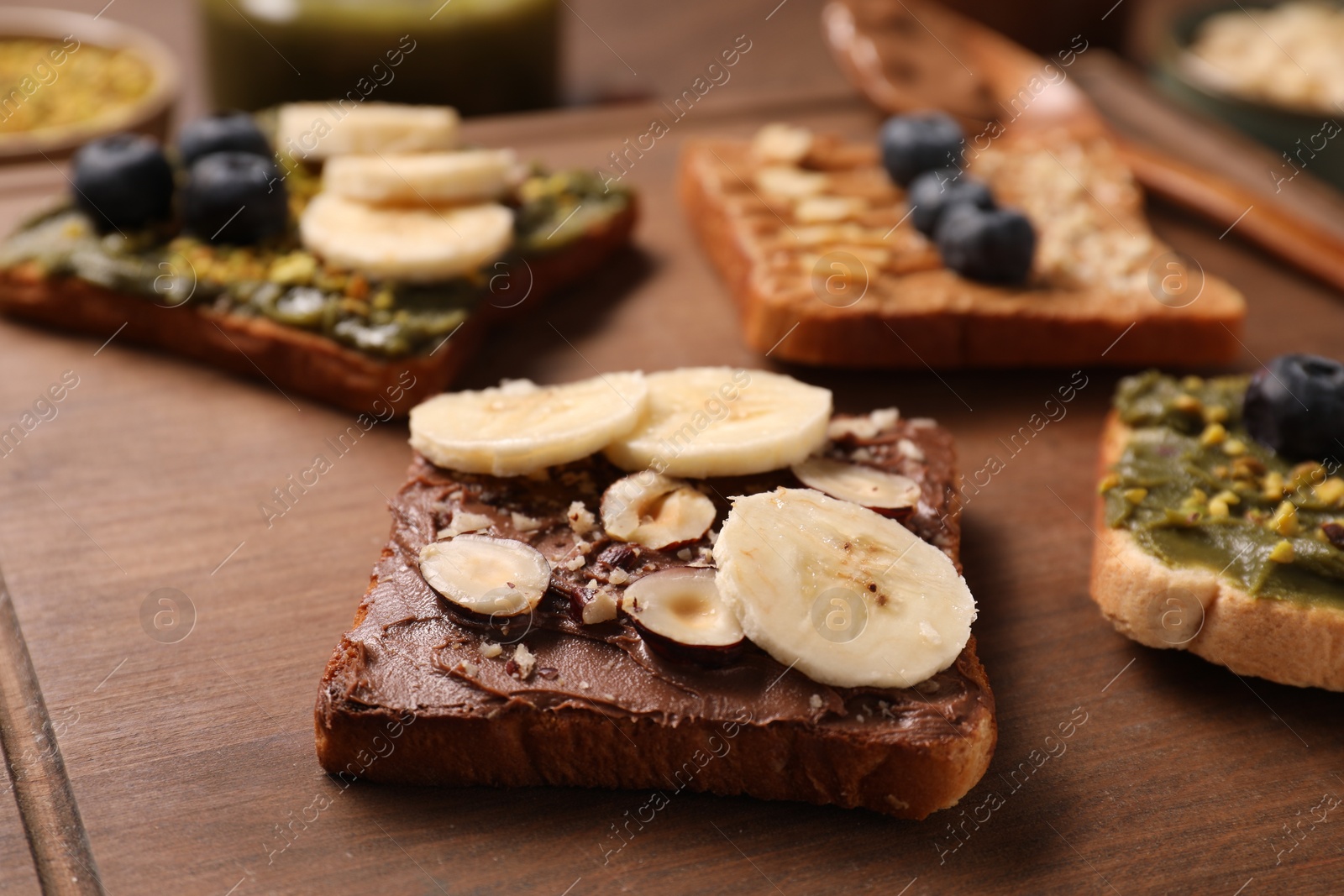 Photo of Toasts with different nut butters, banana slices, blueberries and nuts on wooden board, closeup