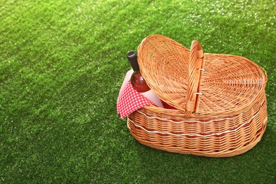 Picnic basket with bottle of wine on grass, space for text