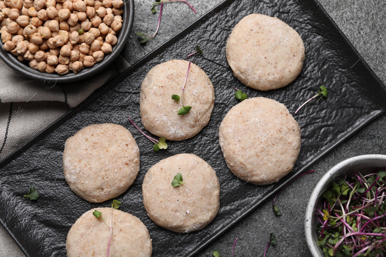 Photo of Raw vegan nuggets, greens and chickpeas on grey table, flat lay