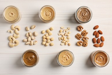 Many tasty nut butters in jars and nuts on white wooden table, flat lay