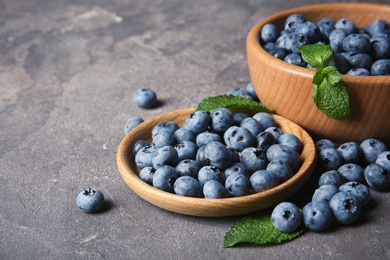 Dishware with juicy blueberries and green leaves on color table