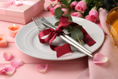 Photo of Place setting with roses and candles on pink table, closeup. Romantic dinner