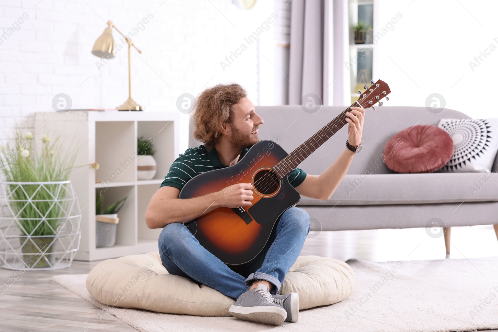 Photo of Young man playing acoustic guitar in living room