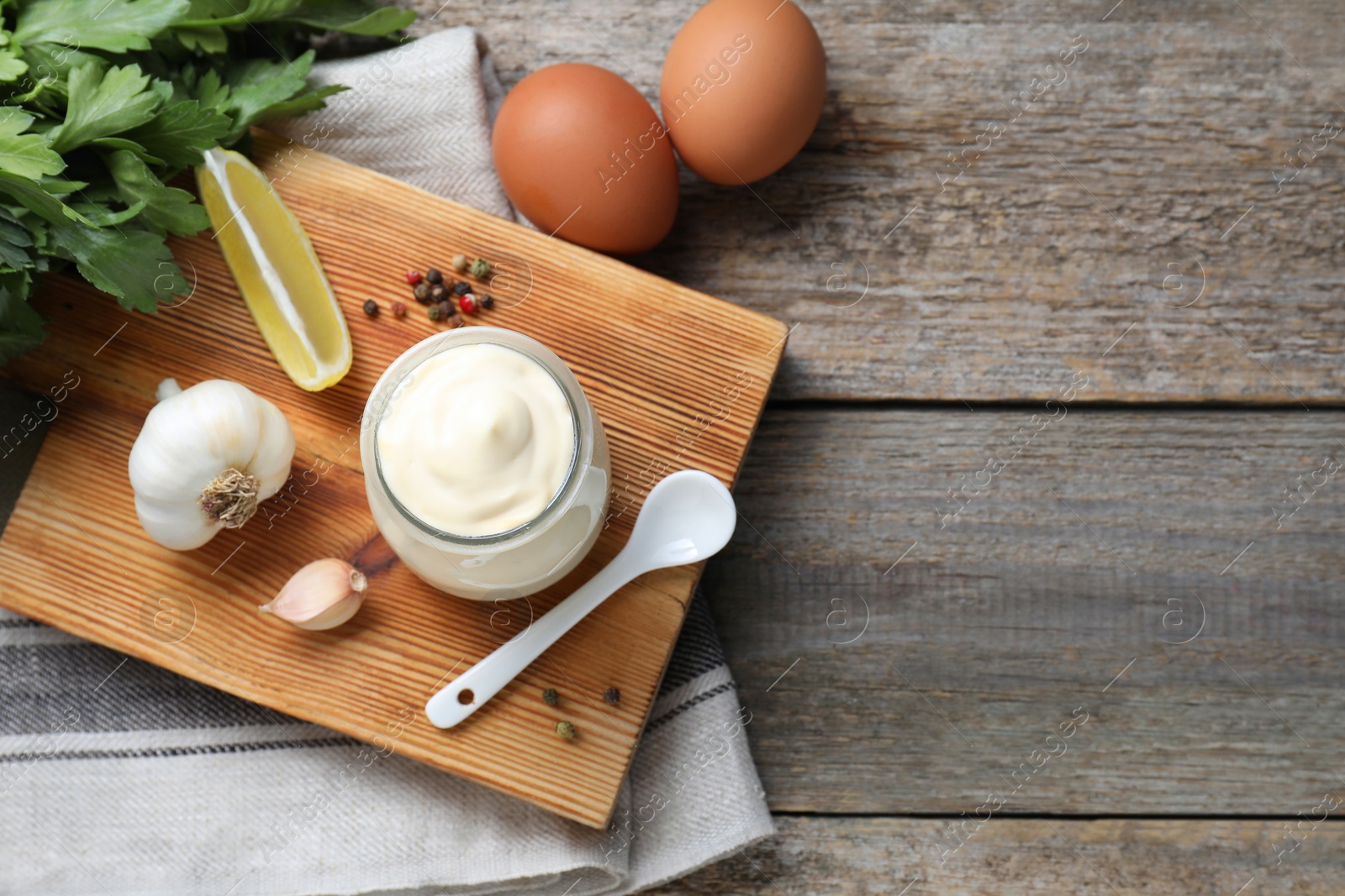 Photo of Fresh mayonnaise sauce in glass jar and ingredients on wooden table, flat lay. Space for text