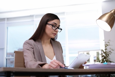 Photo of Businesswoman working with tablet and documents at table in office