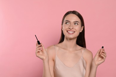 Young woman with eyelash oil on pink background, space for text