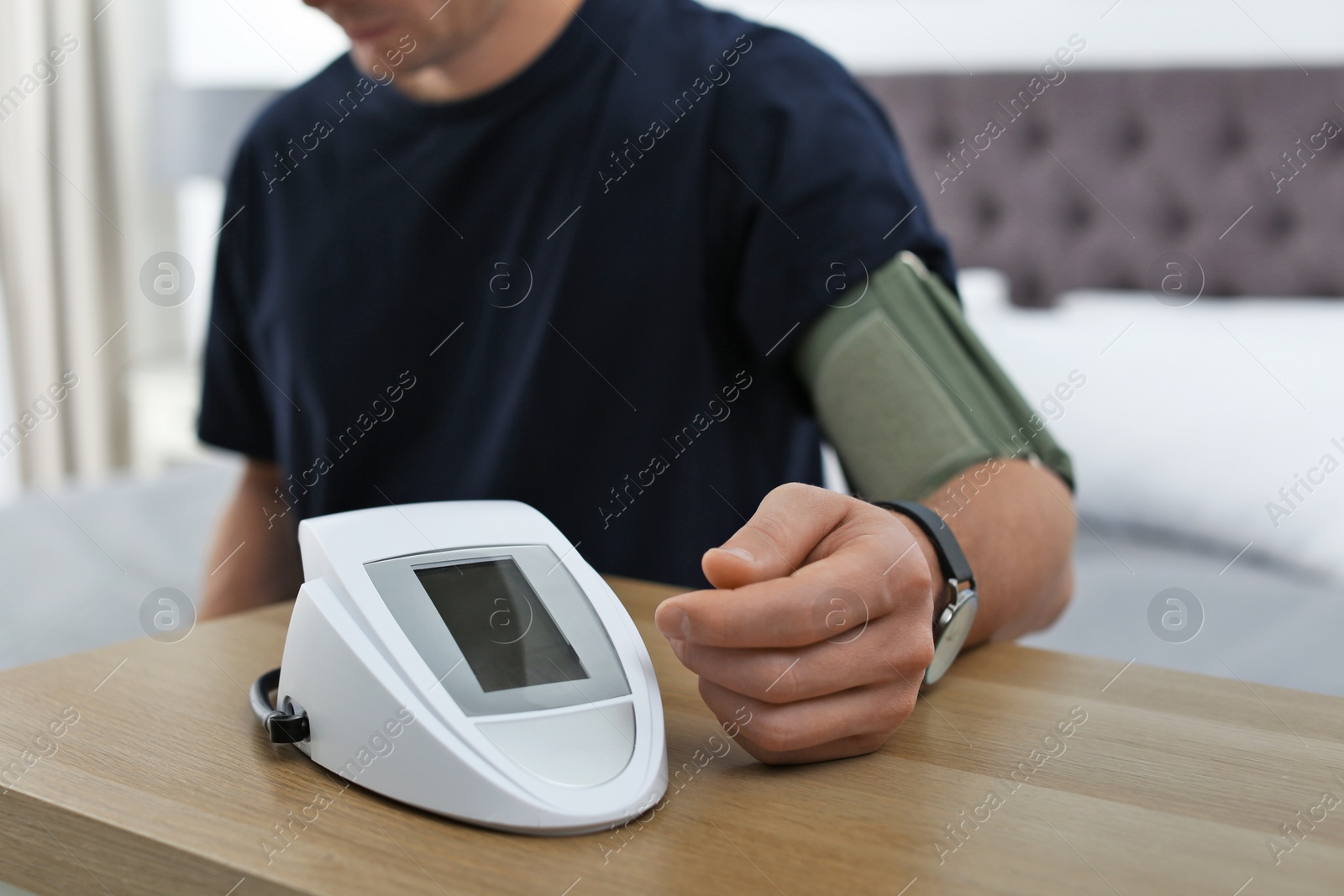 Photo of Man checking blood pressure with sphygmomanometer at table indoors, closeup. Cardiology concept