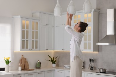 Photo of Woman changing lightbulb in ceiling lamp at home
