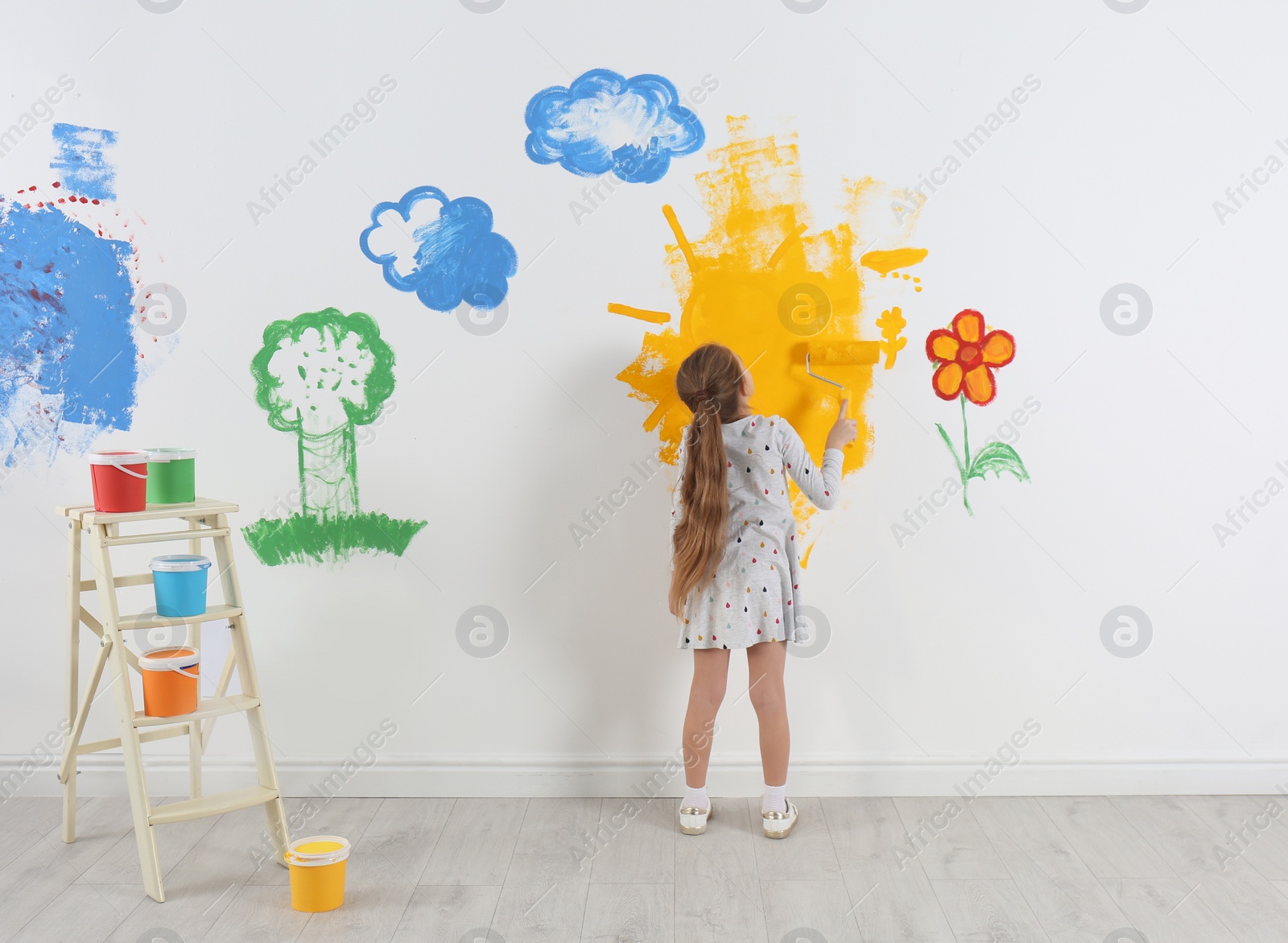 Photo of Little child painting wall with roller brush indoors