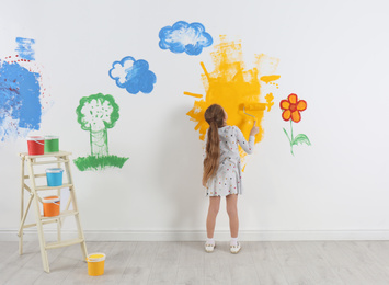 Photo of Little child painting wall with roller brush indoors