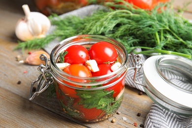 Photo of Pickled tomatoes in glass jar and products on wooden table