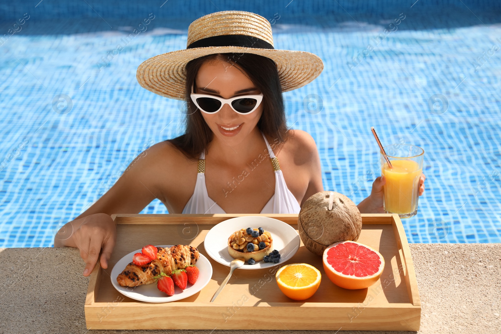Photo of Young woman with delicious breakfast on tray in swimming pool