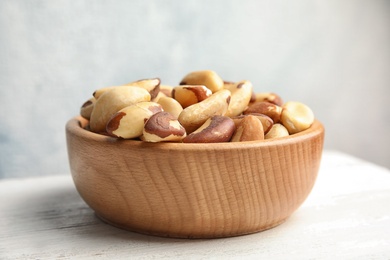 Bowl with tasty Brazil nuts on white table