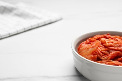 Bowl of spicy cabbage kimchi on white marble table, closeup. Space for text