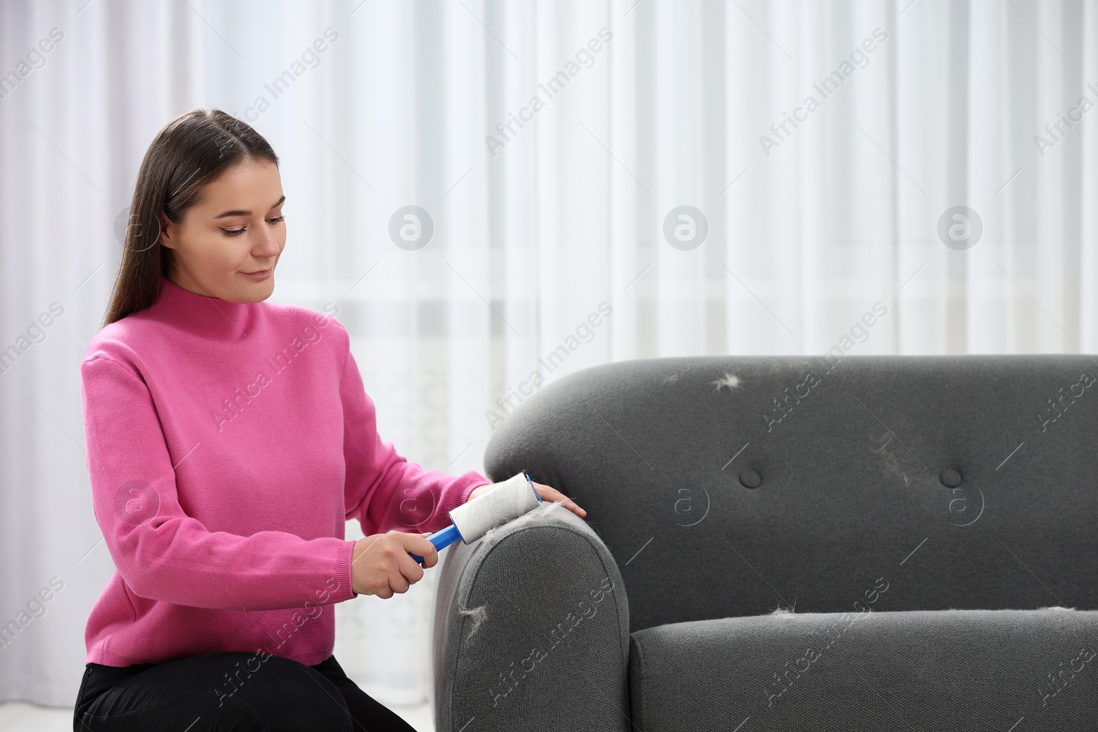 Photo of Woman with lint roller removing pet hair from sofa at home