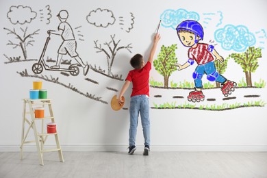 Image of Little boy drawing his dreams on wall, back view